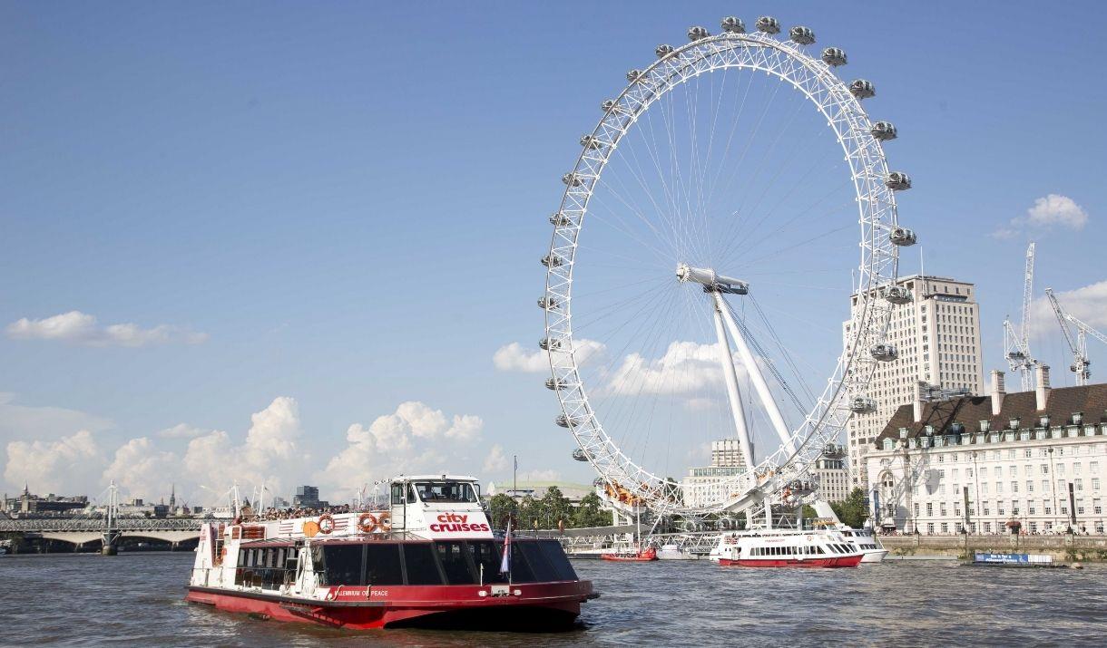 Red and white City Cruises boat on the River Thames passing the London Eye