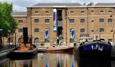 Museum of London Docklands building by the river with small boats taxied in front of it.