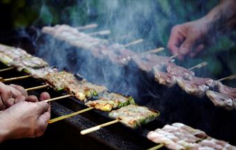 Small wooden sticks of meat, fish and cheese being grilled over open flame at Sticks'n'Sushi.