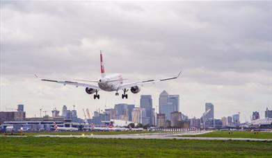 A plane comes in to land at London City Airport with Canary Wharf in the background.