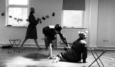Three dancers in dressing gowns rehearsing in an almost empty room.