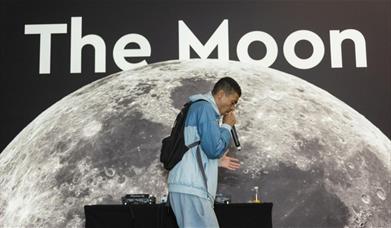 Youth artist with a mic in his hand facing right side in front of 'The Moon' banner.