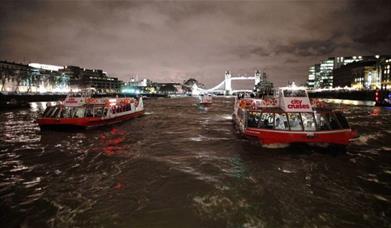 Two City Cruises boats on river Thames at night with lit up Tower Bridge in the background.