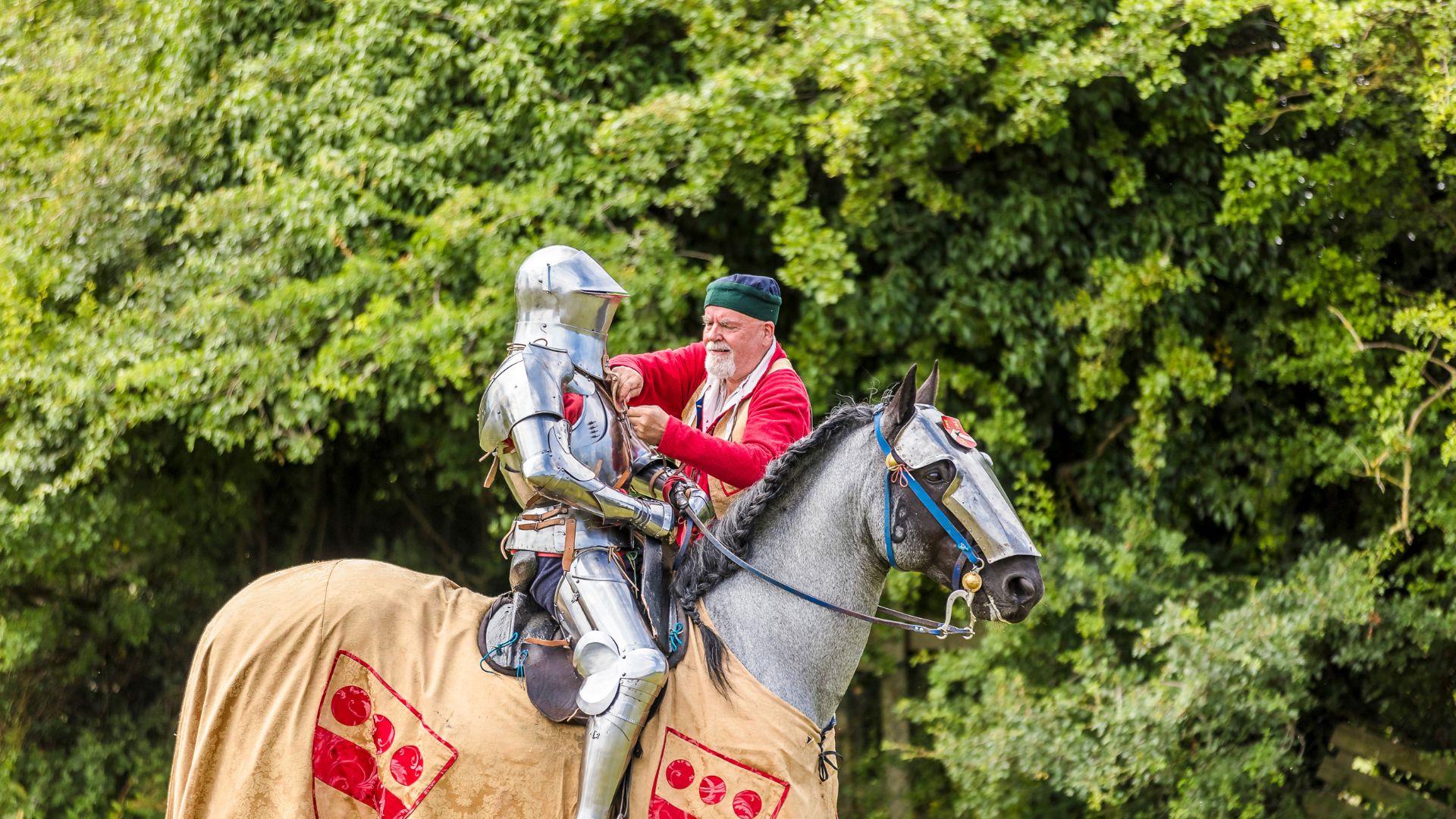 A knight on a horse being aided by a helper.