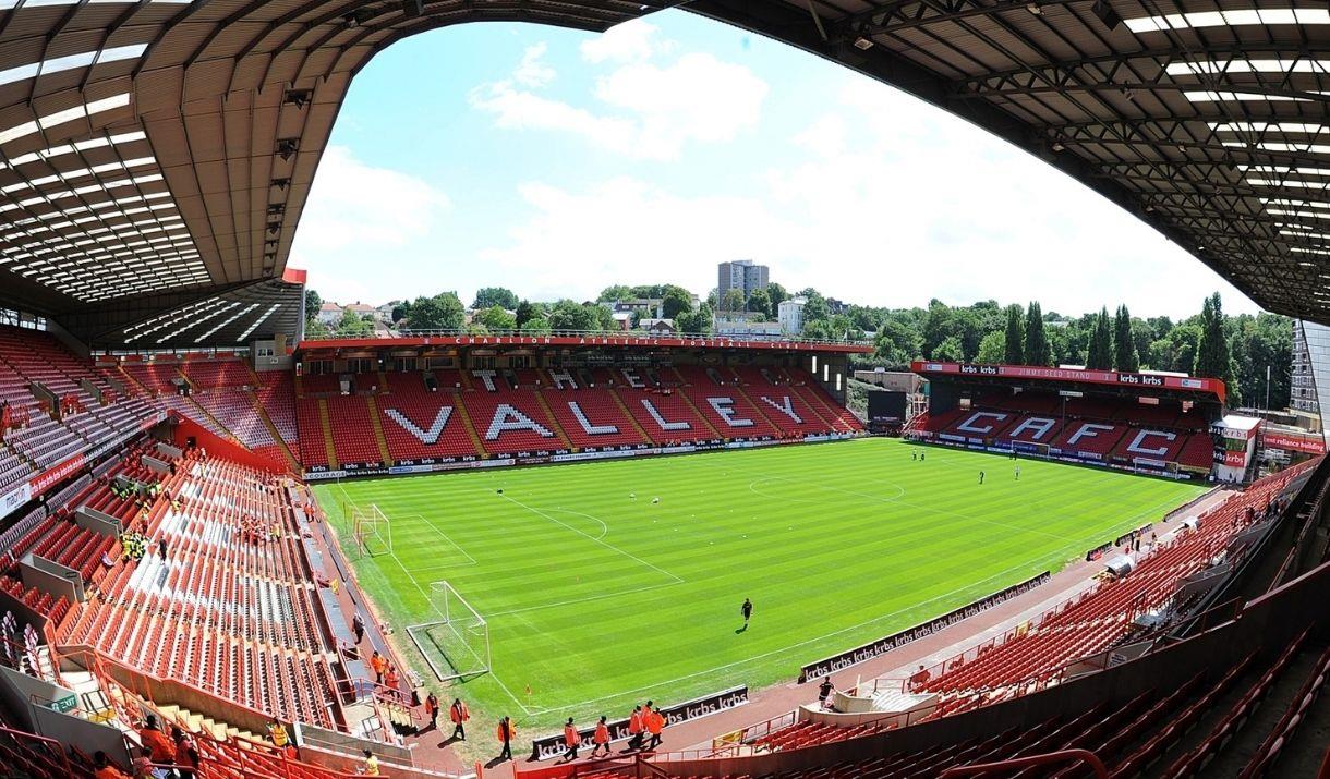 Image shows players in action inside the stadium with red seating all round.