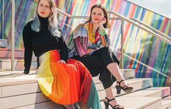 Artist Liz West and Designer Kitty Joseph adorned in her bright colour signature collection in front of the art installation on The Tide.