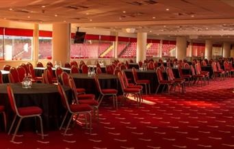 Inside the North Stand Venue at Charlton Athletic, showing rows of Black circular tables with red chairs.