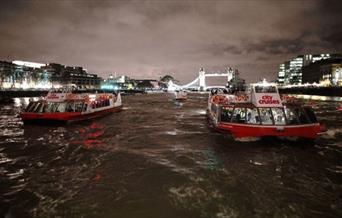Two City Cruises boats on river Thames at night with lit up Tower Bridge in the background.