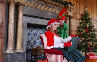 Mrs Claus telling a story in a nice decorated room with an elf.