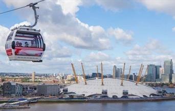 Emirates Air Line Cable Car soaring over the river Thames at dusk, overlooking The O2 and Canary Wharf