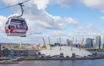 Emirates Air Line carrier on top of river Thames, overlooking The O2 which is a white dome with 12 yellow pillars around on top.