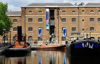 Museum of London Docklands building by the river with small boats taxied in front of it.
