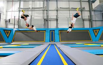 Four children in white t-shirts and black shorts jumping on the variety of interconnected trampolines.