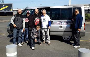 Six tour guides from Satisfaction Tour posing in front of their silver mini coach.