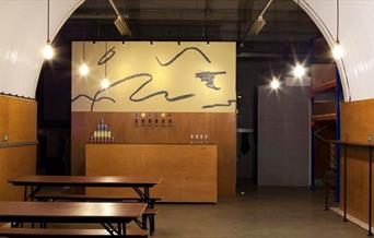 Inside of Villages Taproom Brewery with bar station in the background, benches to the left side and standing table on the right side