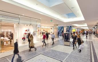 A photo taken inside of the Canary Wharf Shopping centre. Showing a well lighted and visually stunning shopping centre, with lots of shops to visit.