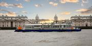 Blue and white City Cruises boat on the River Thames in front of Old Royal Naval College in Greenwich