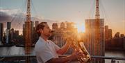 Exclusive Friday night climbs with a twist: refreshing beverage, sky-high sunsets, and live saxophonist performance playing classic summertime tunes