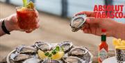 Friends enjoying oysters and Bloody Marys at a trendy Greenwich riverside spot overlooking the London skyline