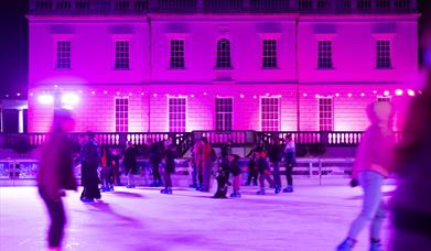 People skating in an illuminated ice rink in front of  Queen's House in Greenwich