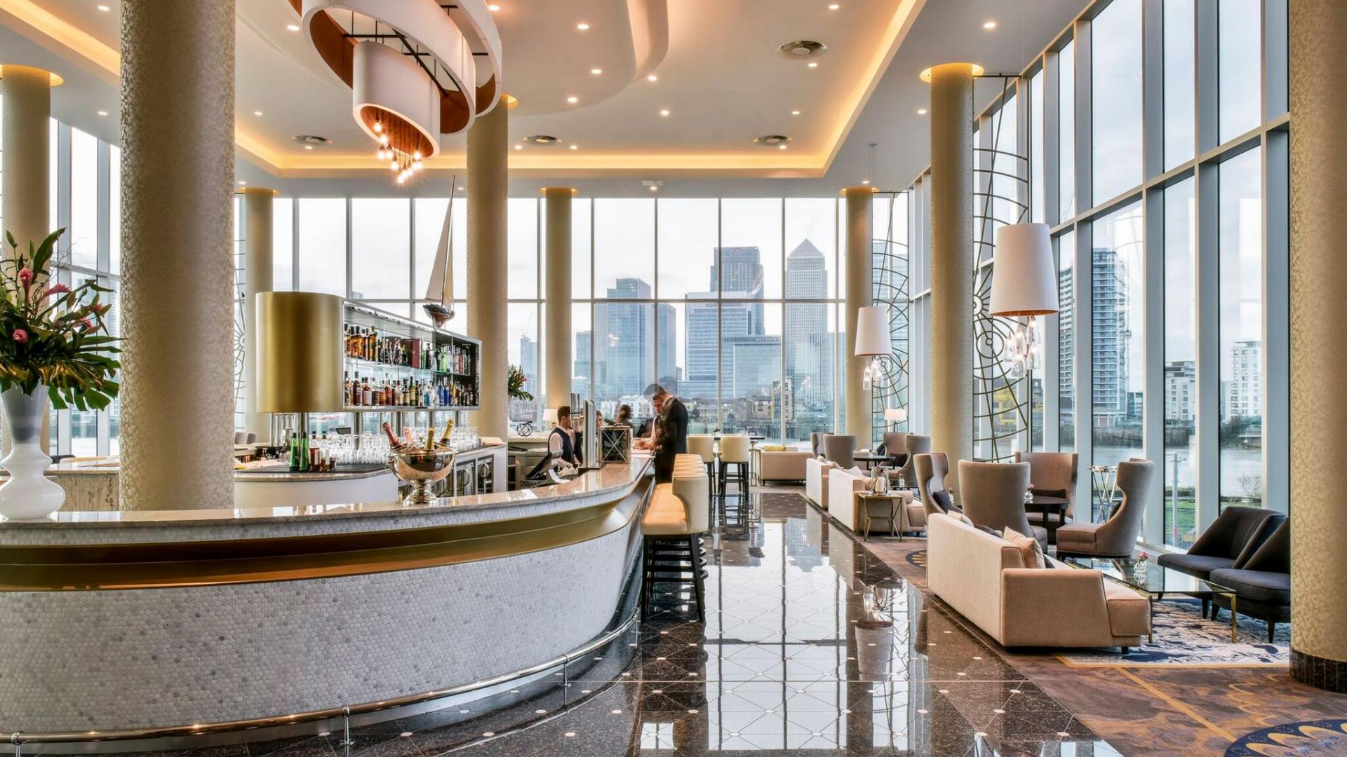 The beautiful interior of the Clipper Bar at the InterContinental London - The O2 on Greenwich Peninsula with central bar and floor to ceiling windows and views of the river and Canary Wharf.