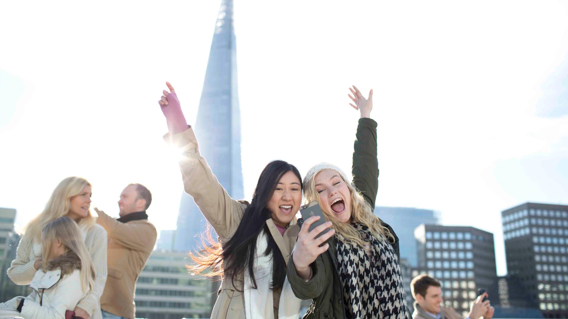 Two girls take a selfie in front of The Shard while on a sightseeing cruise on board a boat on the river Thames.