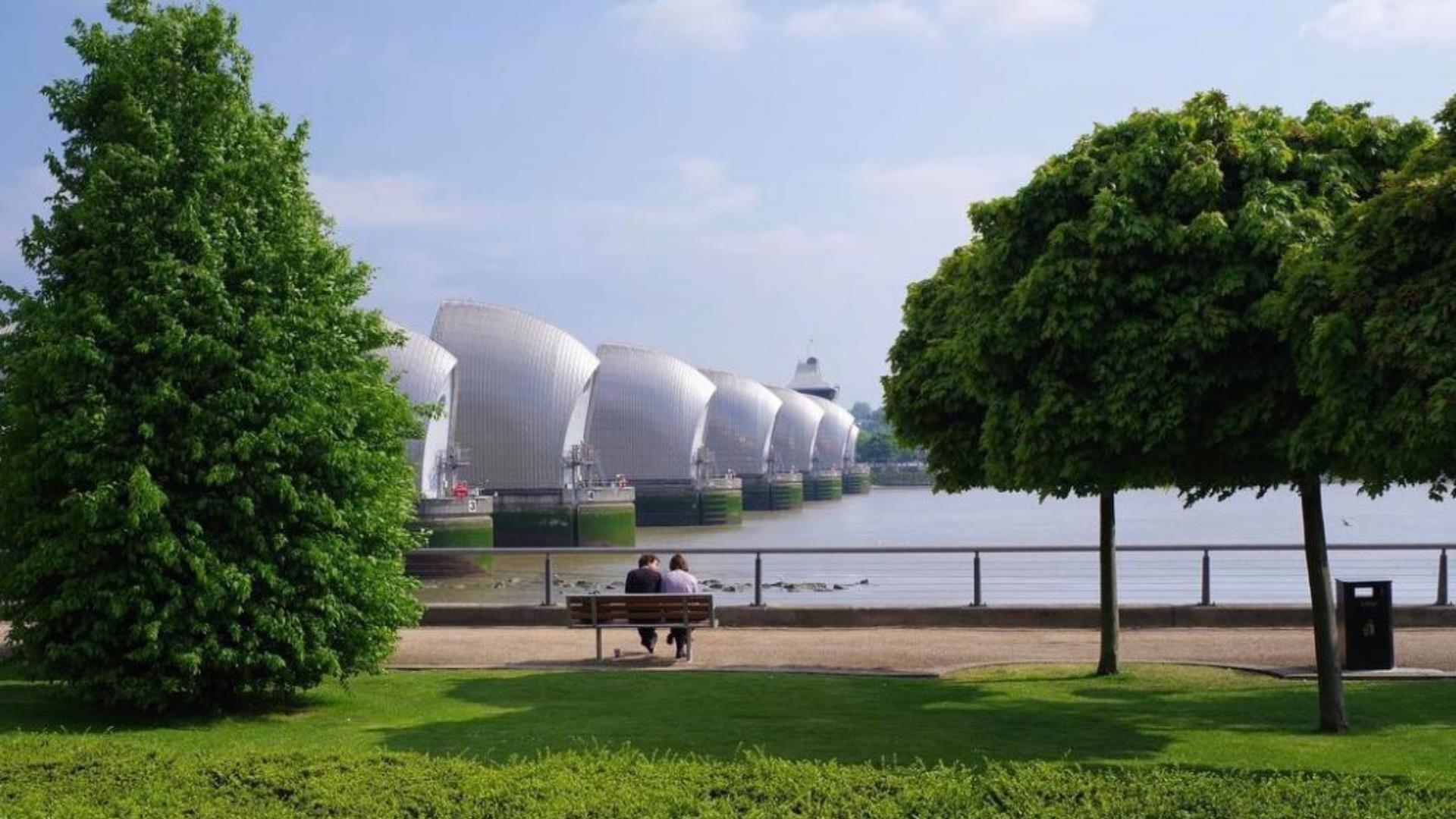 A couple sit beside the river Thames overlooking the Thames Barrier.