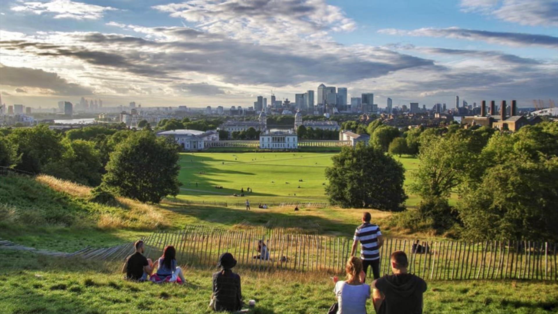 People sitting down in Greenwich Park looking at the view.