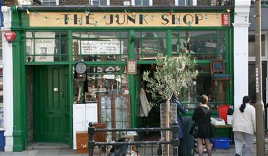 A photo taken outside The Junk shop in Greenwich. Showing a green shop filled with antiques and collectables.