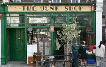 A photo taken outside The Junk shop in Greenwich. Showing a green shop filled with antiques and collectables.