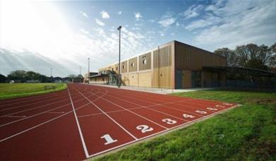 A photo taken of Sutcliffe Park Sport Centre's running track, showing a red track surrounded by fields and a building.