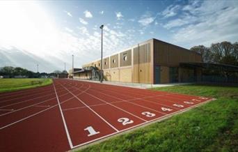 A photo taken of Sutcliffe Park Sport Centre's running track, showing a red track surrounded by fields and a building.