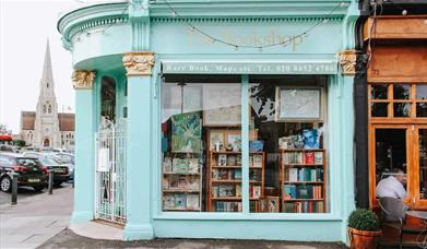 Outside The Bookshop on the Heath in Blackheath. A mint green painted bookshop with a white gate and windows showing a wide range of books.