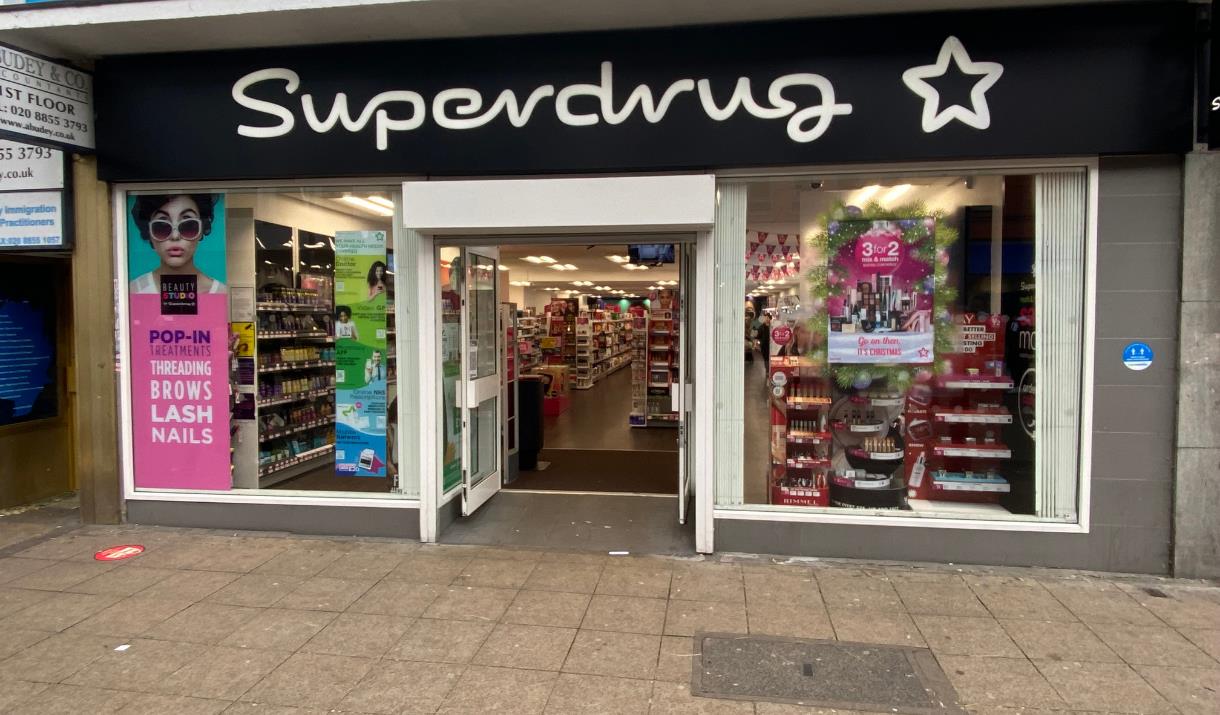 A photo taken outside of Superdrug, Woolwich. Showing a black and white modern shop with a wide range in products.