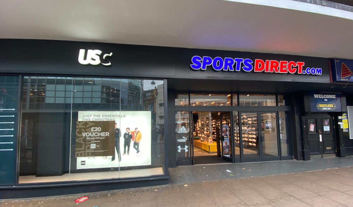 Outside Sports Direct in Woolwich. Showing a black shop front with a red and blue Sports Direct logo.