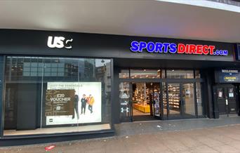 Outside Sports Direct in Woolwich. Showing a black shop front with a red and blue Sports Direct logo.