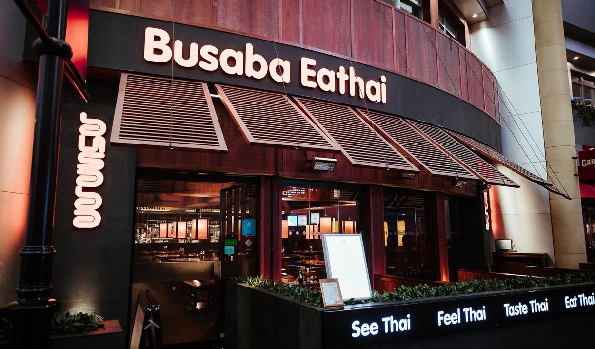 Busaba Eathai entrance in wood finish with wooden windows which are open and has the restaurant name in beige on top. Also has outside seating.