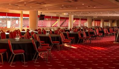 Inside the North Stand Venue at Charlton Athletic, showing rows of Black circular tables with red chairs.