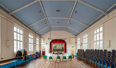Charlton assembly rooms, a large hall with a stage, windows, accessible chairs and a raised ceiling.