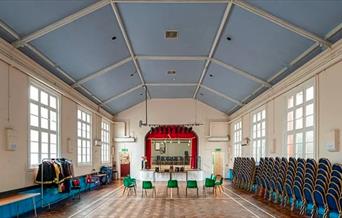Charlton assembly rooms, a large hall with a stage, windows, accessible chairs and a raised ceiling.