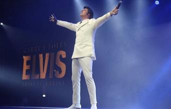 Elvis lookalike wearing white outfit performing onboard City Cruises Elvis Tribute Cruise with blue background.