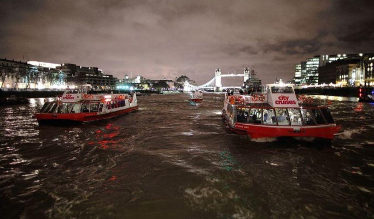 Two City Cruises boats on river Thames at night with lit up Tower Bridge in the background.