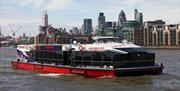 City Cruises boat on river Thames with London skyline in the background.