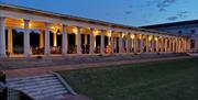People sat at round tables on the Colonnades, Royal Museums Greenwich Grounds in the evening