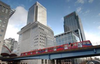 Docklands Light Railway train moves along a bridge among the skyscrapers of Canary Wharf.