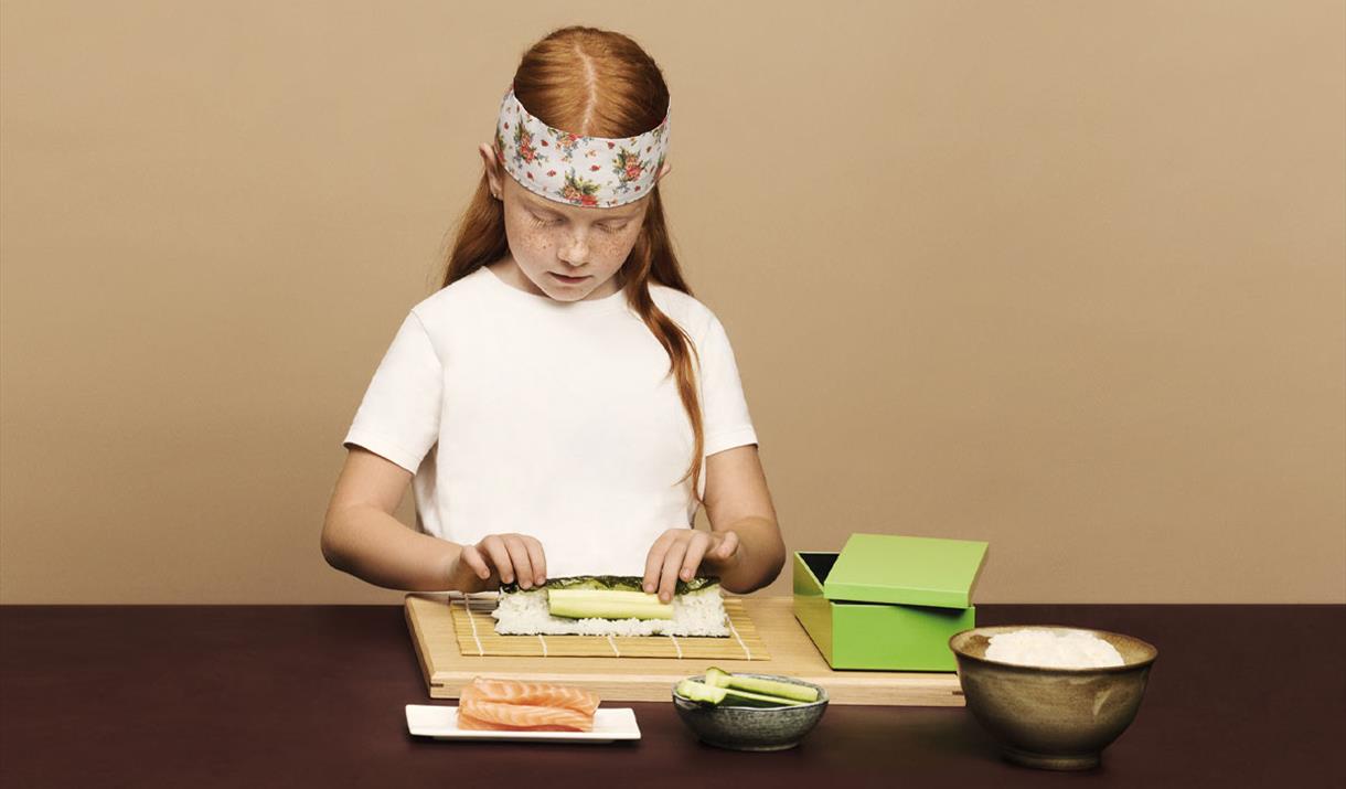 A child rolling sushi with some ingredients set up in front of her