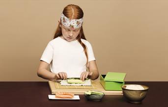 A child rolling sushi with some ingredients set up in front of her
