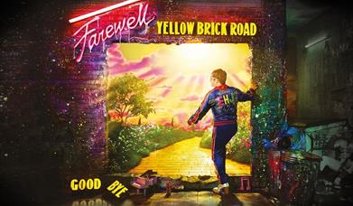 Elton John wearing blue sportswear with pink stripes, standing by the brick wall in the artwork for the Farewell Yellow Brick Road Tour.