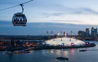 Emirates Air Line Cable Car soaring over the river Thames at dusk, overlooking The O2 and Canary Wharf