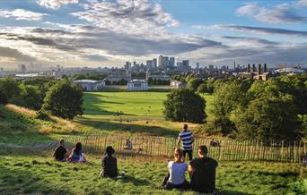 People sitting in Greenwich Park overlooking the view of Greenwich on a summer's evening.